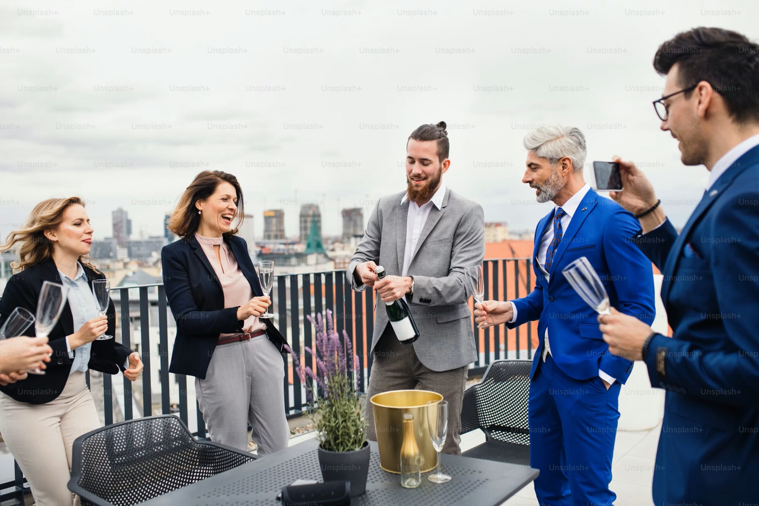 Men And Women Standing On Balcony Opening Champagne